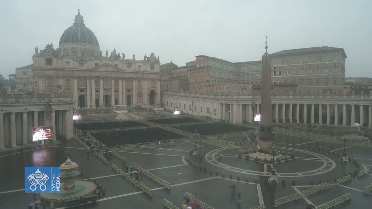 A wide view of St. Peter's Square in Vatican City on a rainy day, showing St. Peter's Basilica and the surrounding colonnades with many chairs set up in the square.