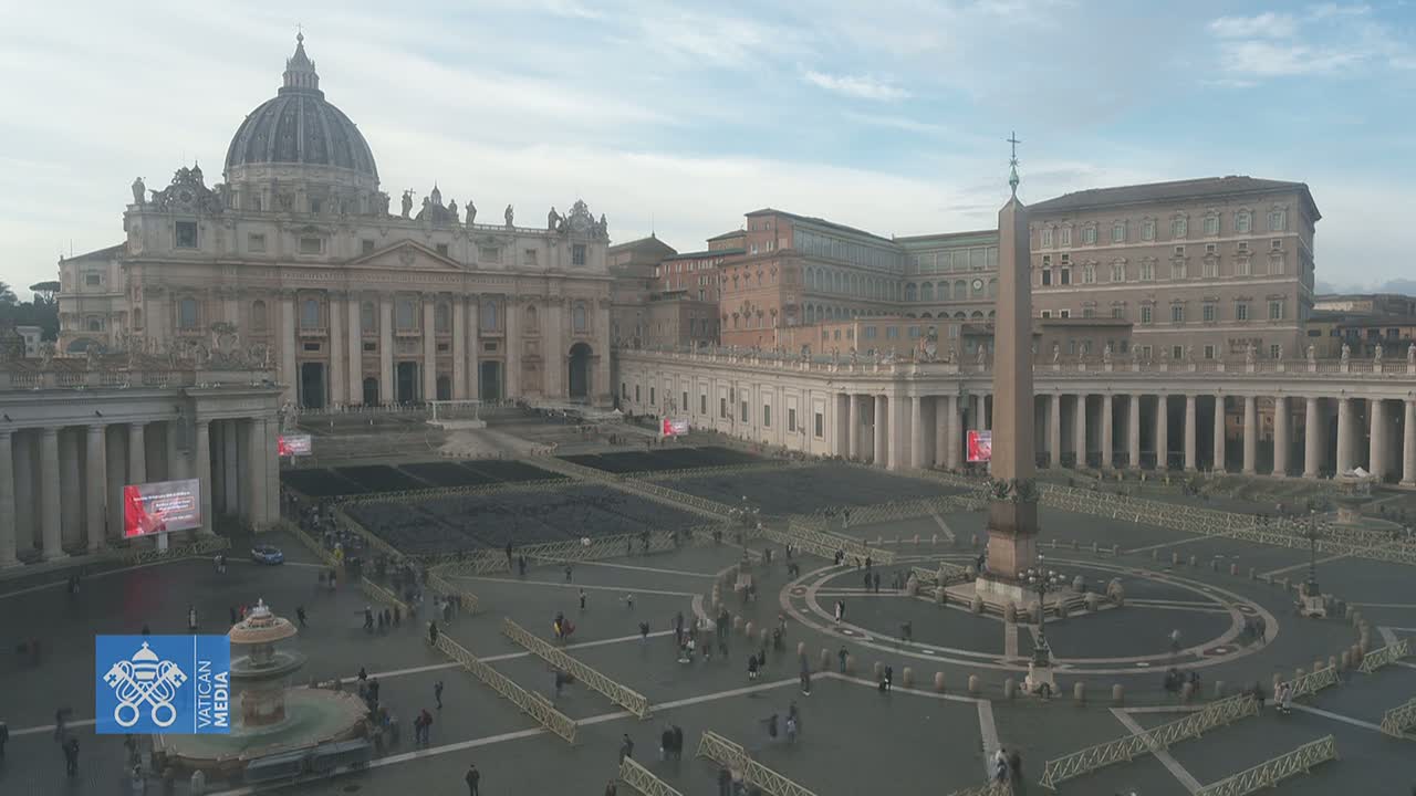 St. Peter's Basilica and St. Peter's Square in Vatican City are shown on an overcast day, with many people sparsely scattered throughout the square and numerous barriers set up.