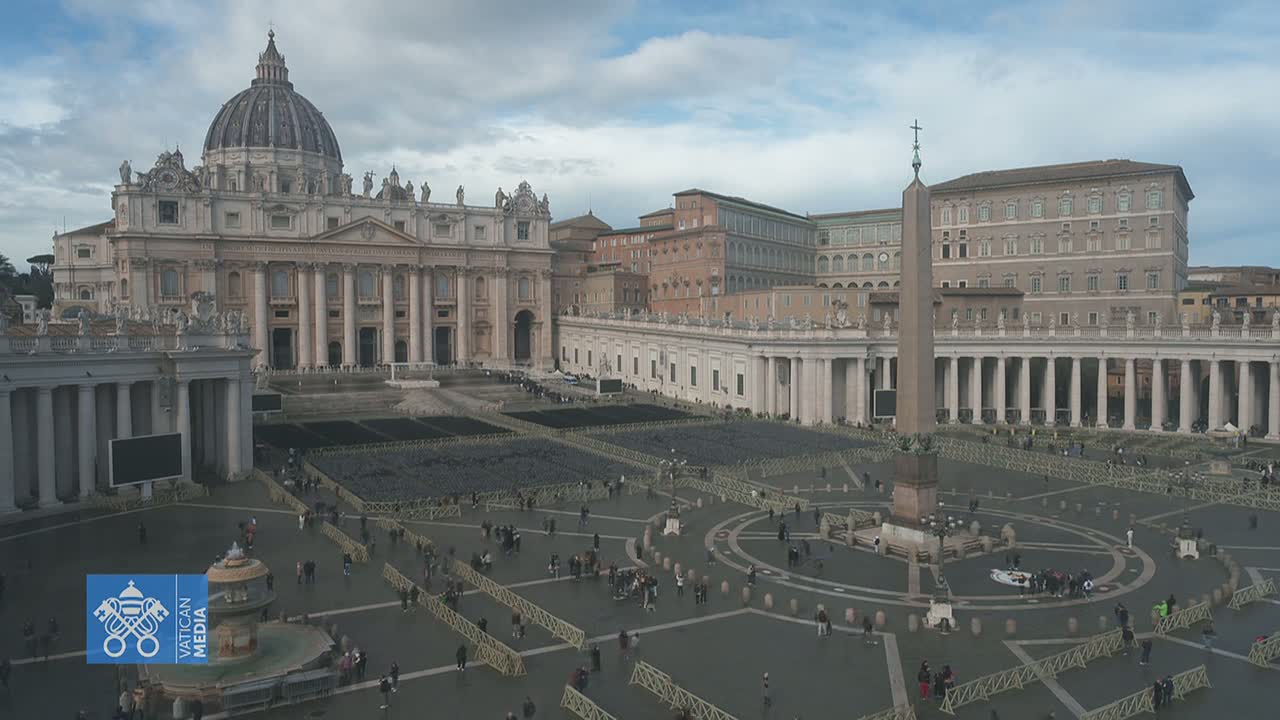 St. Peter's Basilica and St. Peter's Square in Vatican City, under a cloudy sky, with a large crowd of people sparsely spread across the square.