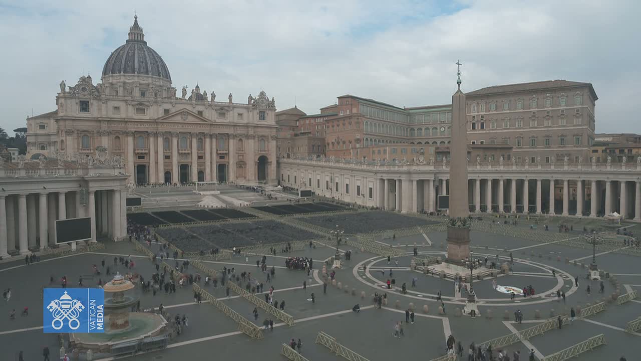 An overcast day reveals St. Peter's Basilica and St. Peter's Square in Vatican City, with numerous people scattered throughout the plaza.