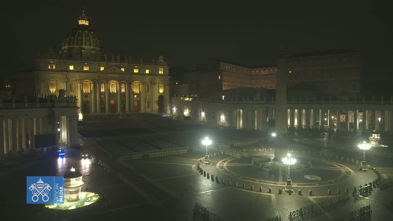 St. Peter's Basilica and St. Peter's Square are illuminated at night, with a wet, empty square and several light posts.