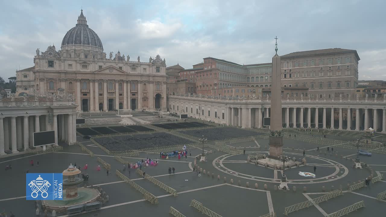 St. Peter's Basilica and St. Peter's Square are seen from an aerial view on an overcast day, with temporary barriers and a few people scattered throughout the square.