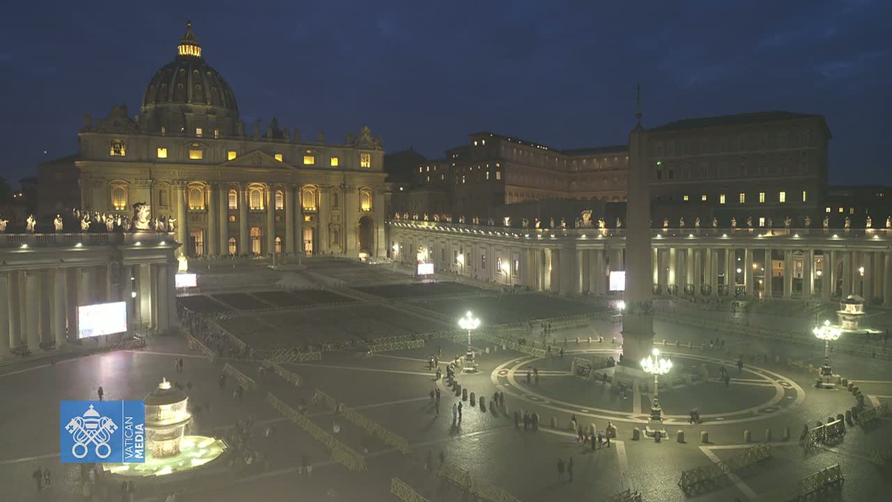 St. Peter's Basilica and Square at night, illuminated, with a few people present.
