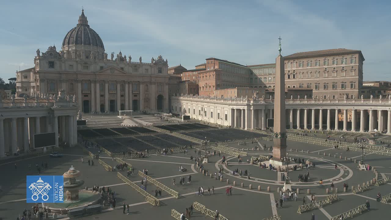 St. Peter's Basilica and St. Peter's Square are shown on a clear day with many people scattered throughout the square and many chairs set up in rows.
