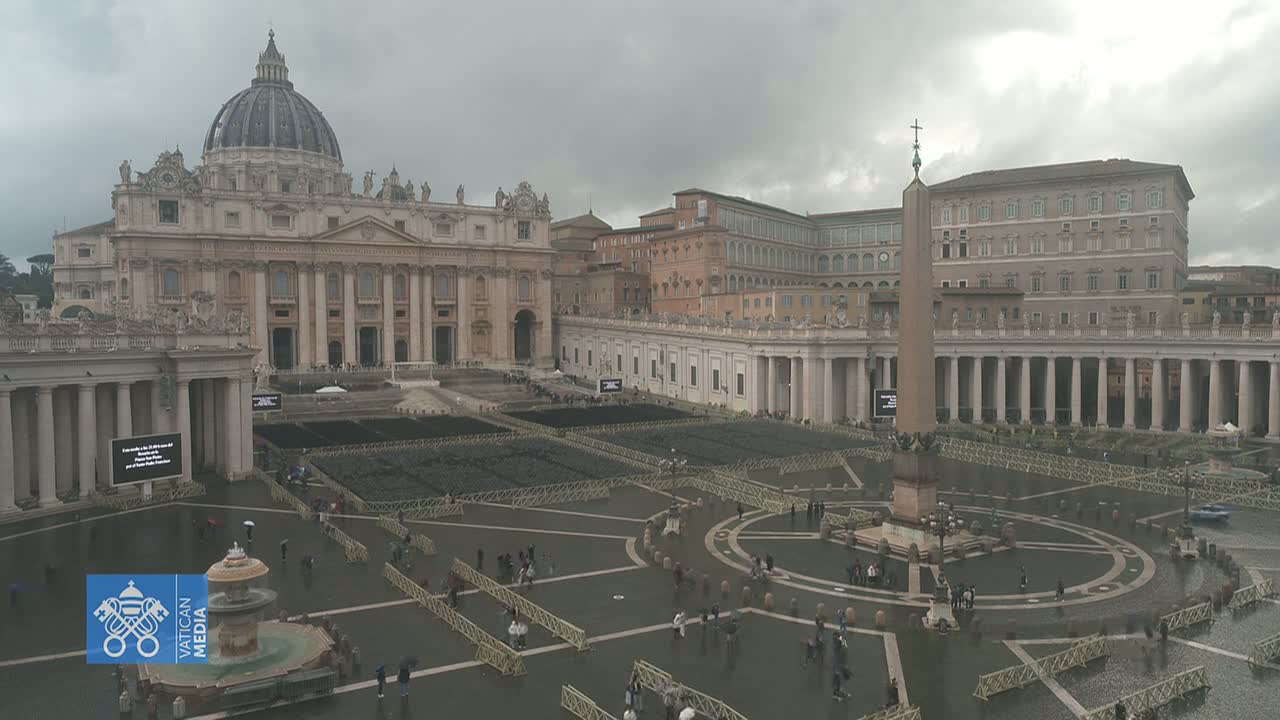 St. Peter's Square in Vatican City on a cloudy, wet day, shows the Basilica and surrounding colonnades with people sparsely scattered across the plaza.
