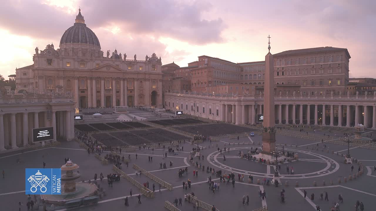 St. Peter's Square in Vatican City at dusk, with many people gathered around the obelisk and St. Peter's Basilica.
