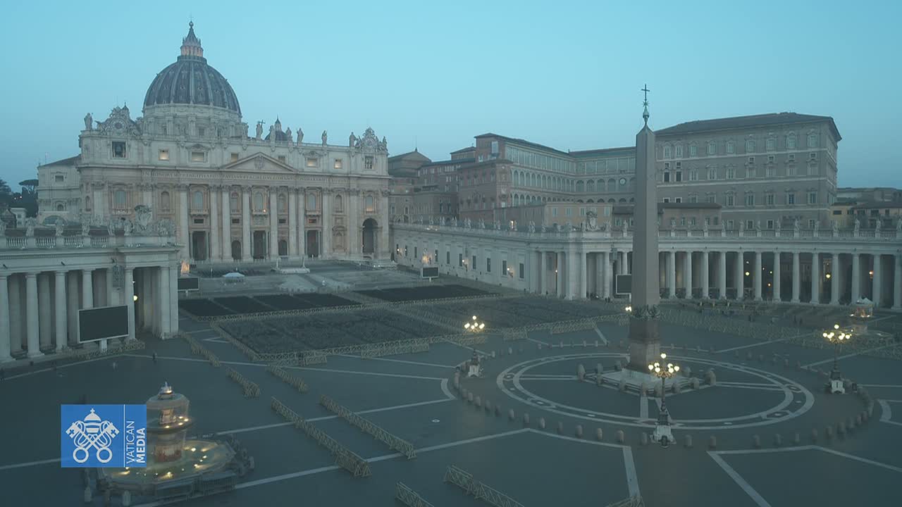 St. Peter's Basilica and Square in Vatican City are shown at dusk, under a clear, pale blue sky.