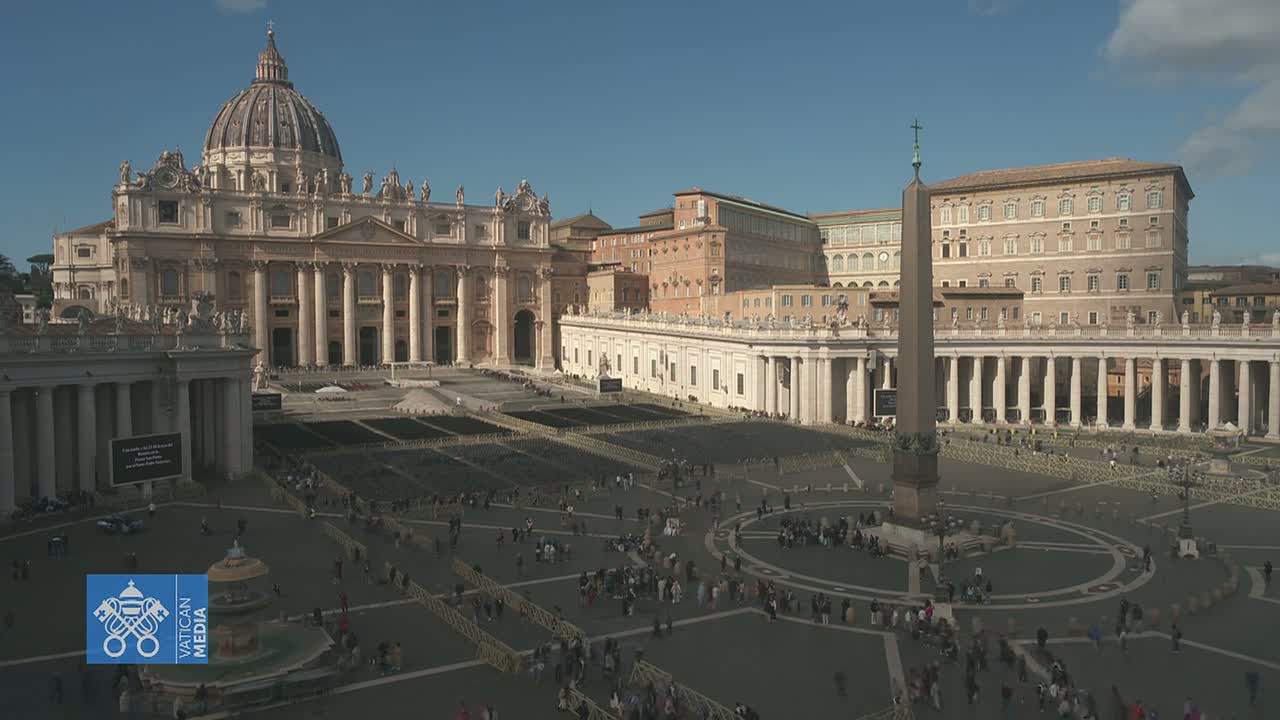 St. Peter's Basilica and St. Peter's Square in Vatican City are shown on a sunny day, with many people gathered in the square.