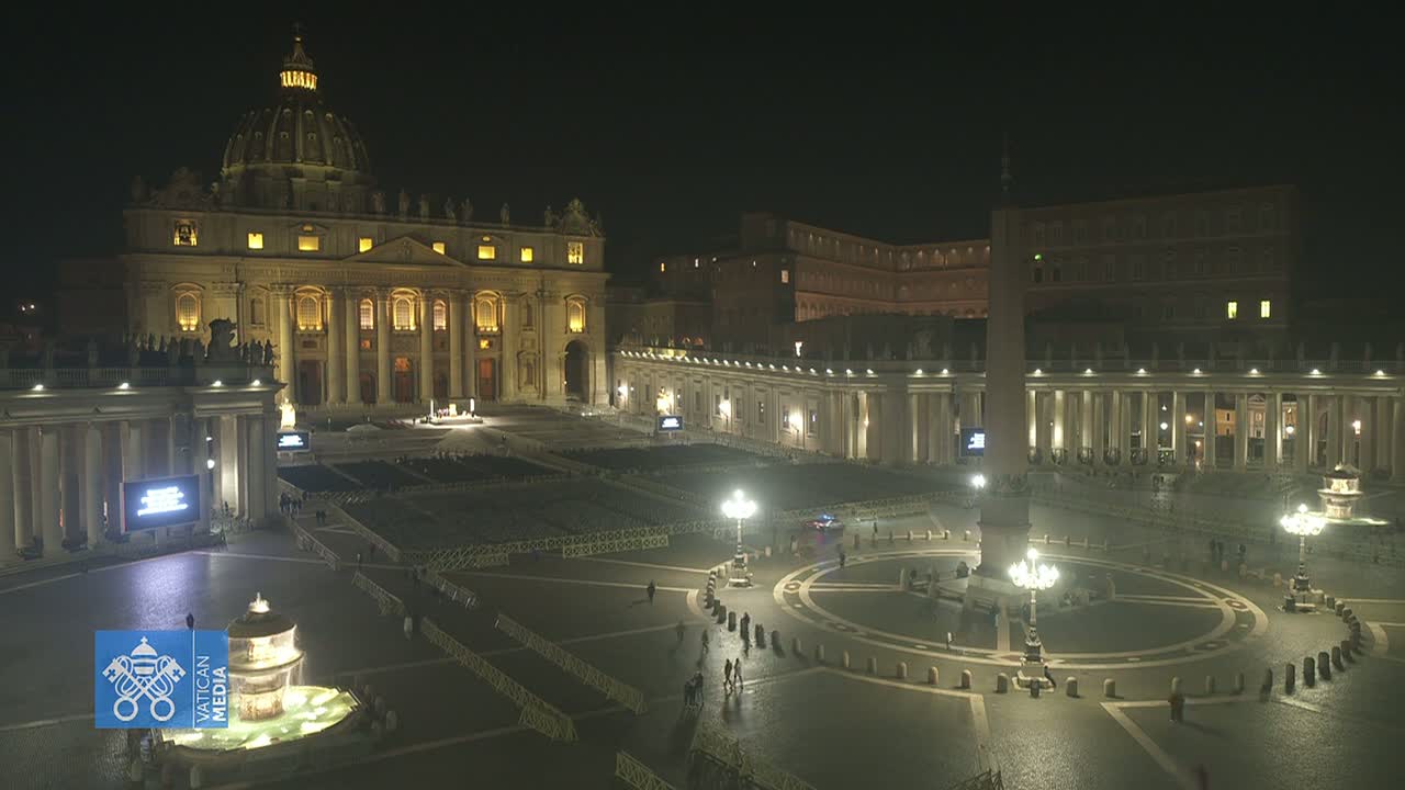 St. Peter's Basilica and Square at night, illuminated, with a few people present.
