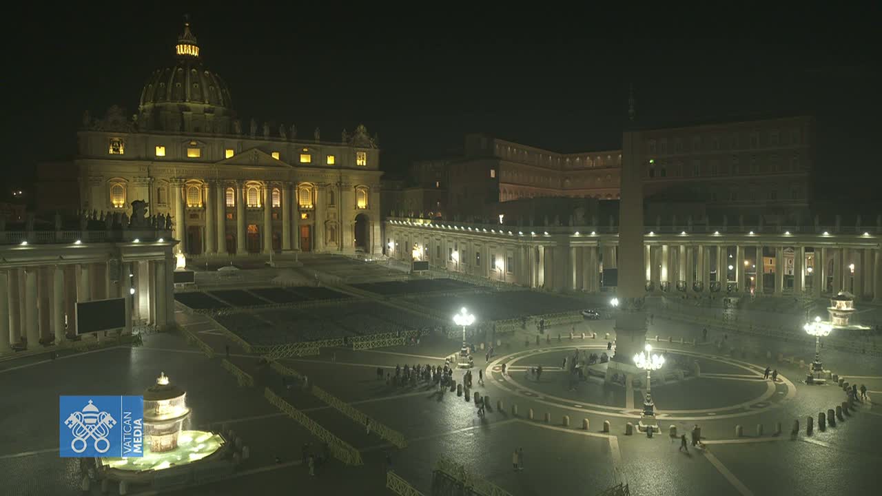 St. Peter's Basilica and St. Peter's Square are illuminated at night, with a few people sparsely scattered across the vast plaza.