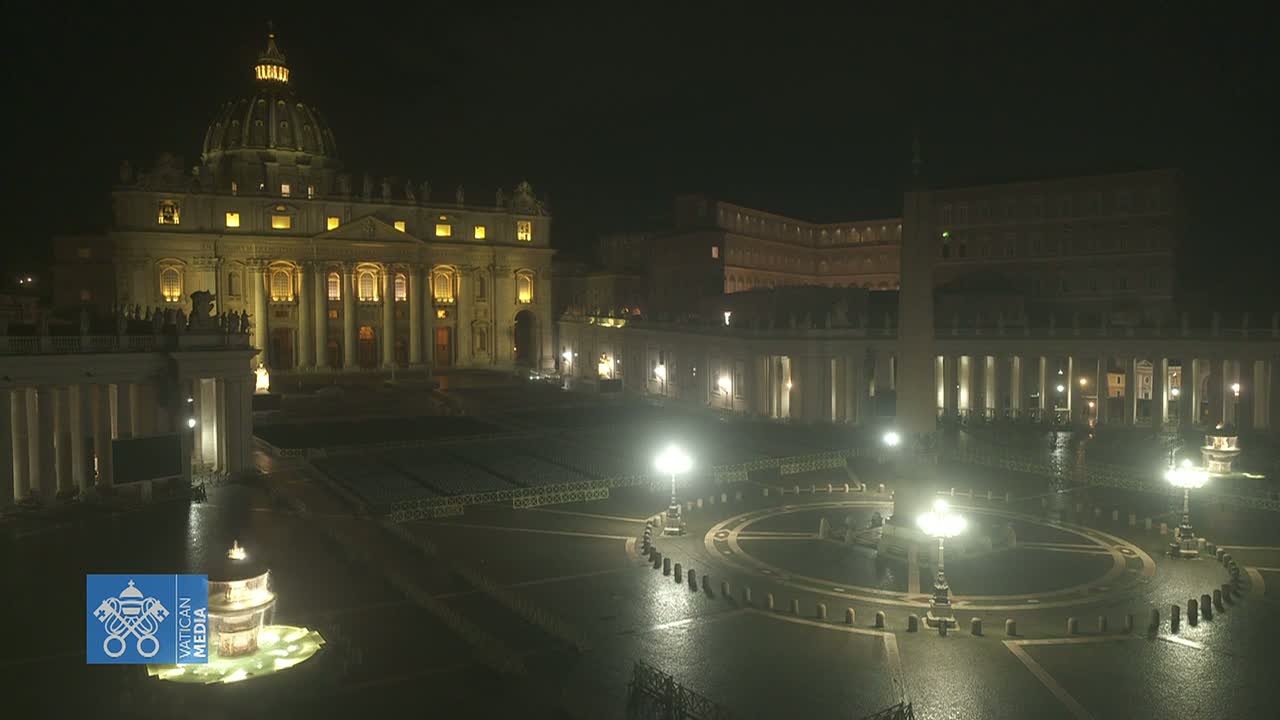 St. Peter's Basilica and Square are illuminated at night under a dark sky, with a wet surface visible in the square.