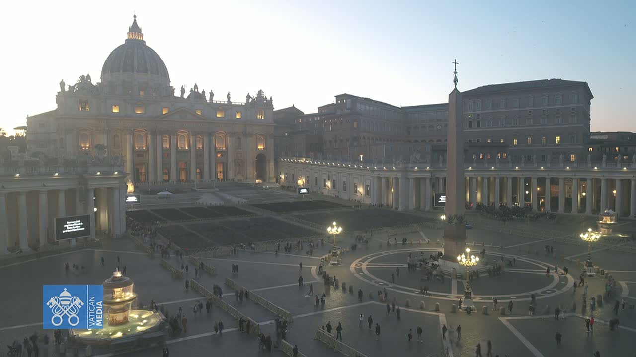 St. Peter's Basilica and St. Peter's Square are shown at dusk, with many people sparsely scattered throughout the square.