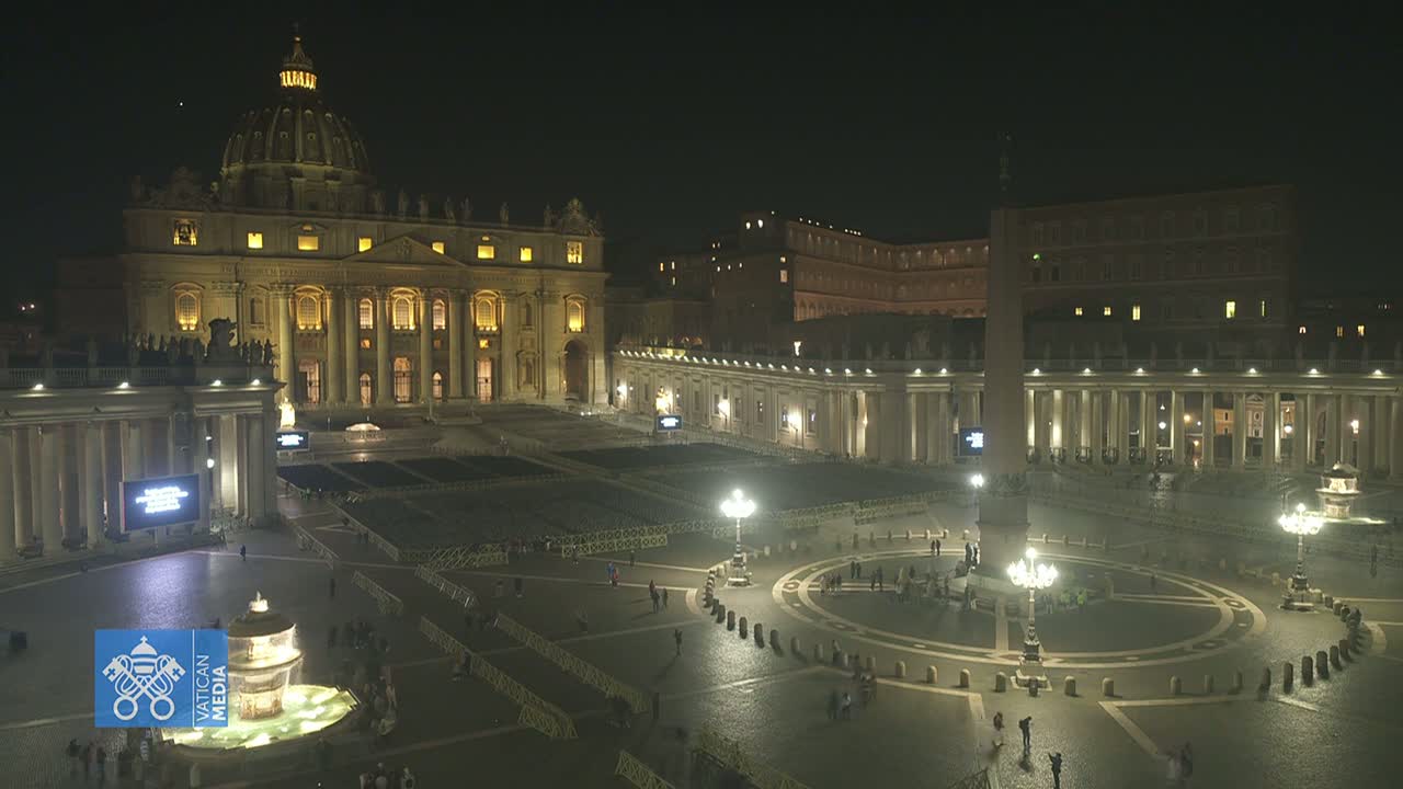 St. Peter's Basilica and St. Peter's Square are illuminated at night, with a few people sparsely scattered across the vast plaza.
