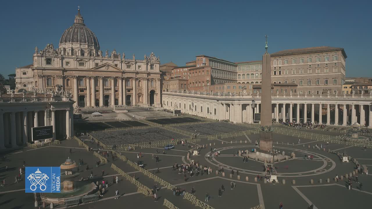 St. Peter's Basilica and St. Peter's Square are shown on a sunny day, with a sparse crowd of people in the square and barriers set up throughout.