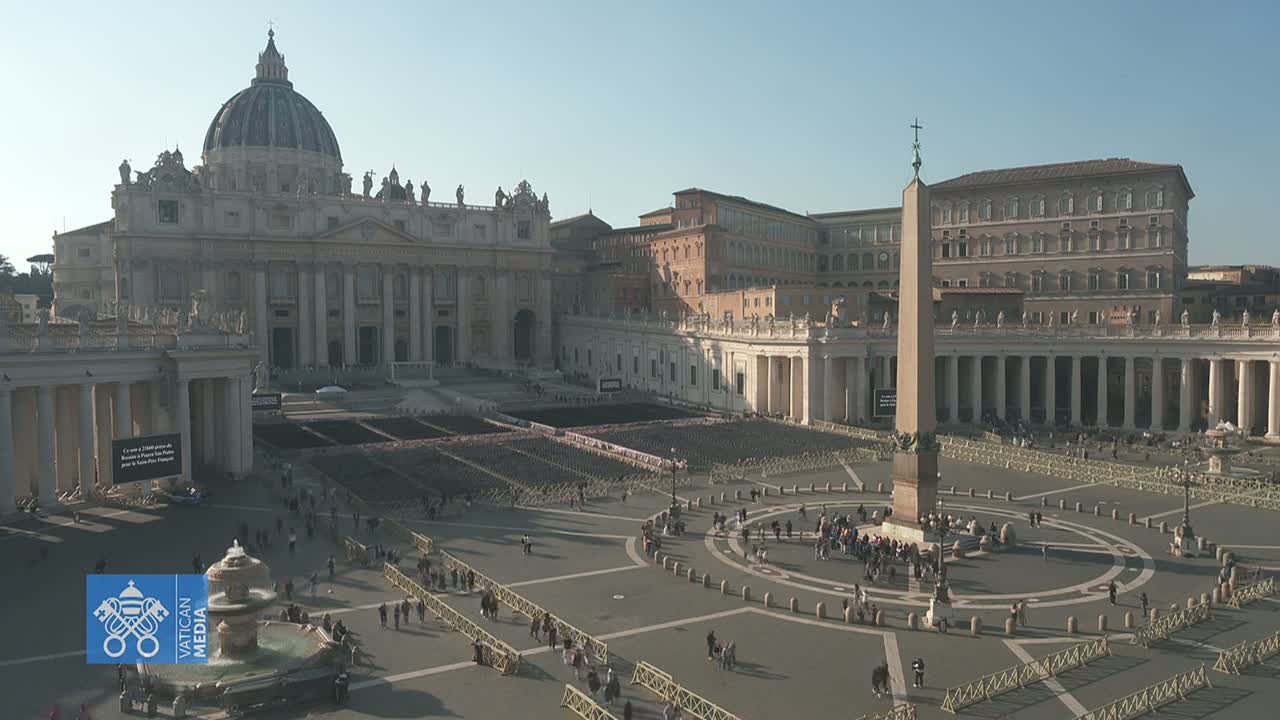 St. Peter's Basilica and Square in Vatican City are shown on a sunny day, with a sparse crowd of people gathered in the plaza.