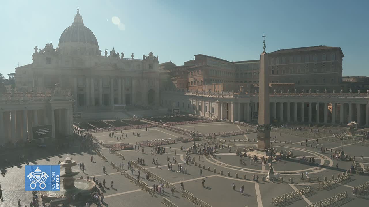 St. Peter's Basilica and Square in Vatican City are filled with people under a hazy, sunny sky.