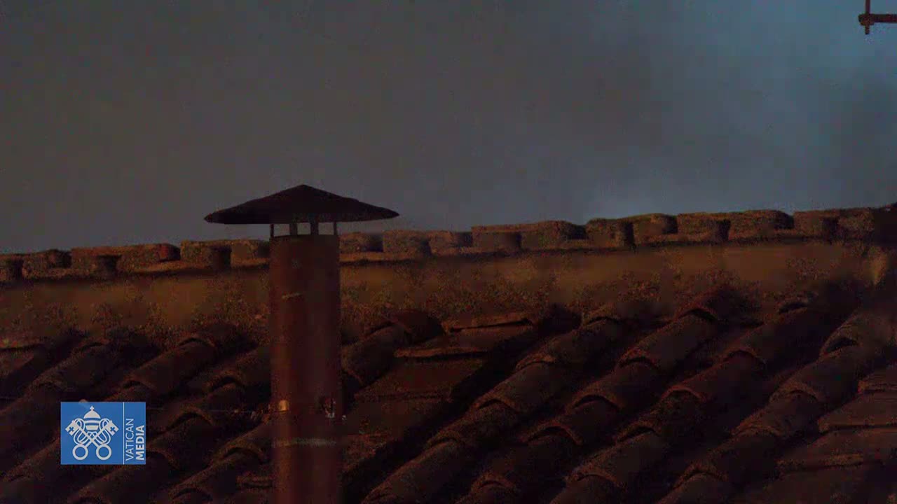 A brown chimney with a cap sits atop a dark brown tiled roof under a twilight sky.