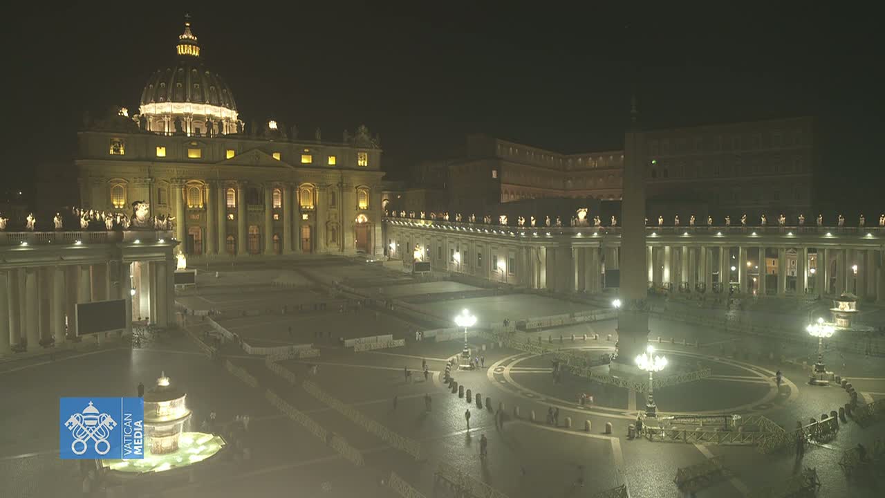 St. Peter's Basilica and square at night, illuminated, with a few people sparsely scattered throughout the large plaza.