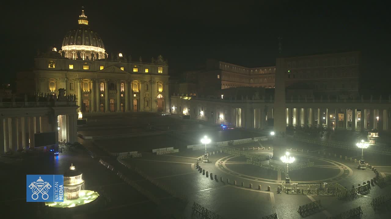 A brightly lit St. Peter's Basilica and square at night, with few people present.
