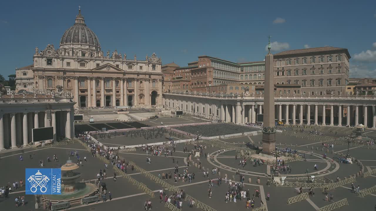 A large crowd gathers in St. Peter's Square under a clear blue sky, surrounding an obelisk and in front of St. Peter's Basilica.