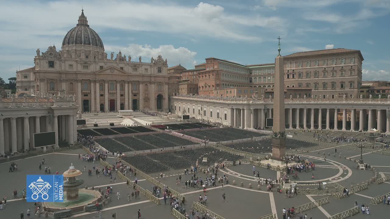 St. Peter's Basilica and St. Peter's Square in Vatican City, under a partly cloudy sky, are filled with many people and seating for a large gathering.