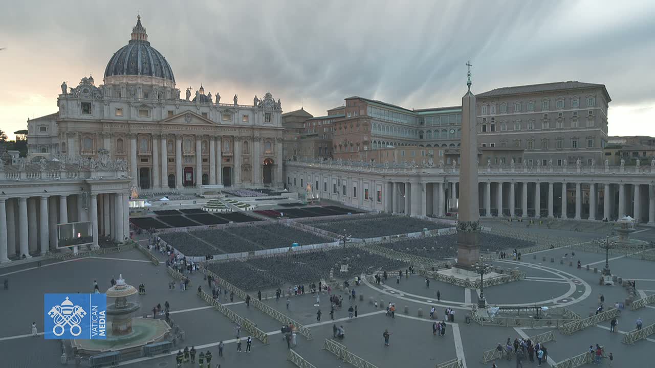 St. Peter's Basilica and Square in Vatican City are shown under an overcast sky, with numerous chairs set up in the square and a few people sparsely scattered throughout.