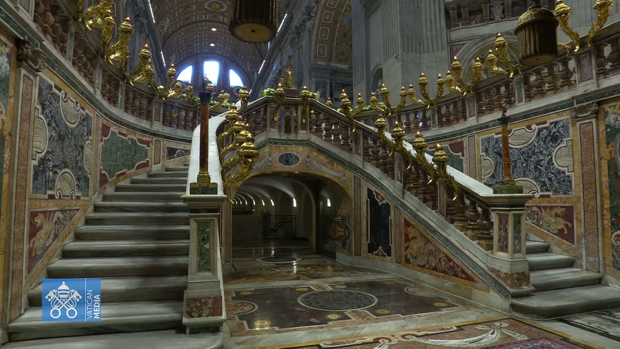 A grand marble staircase with ornate gold railings and multicolored marble inlays curves through an indoor space with arched hallways.
