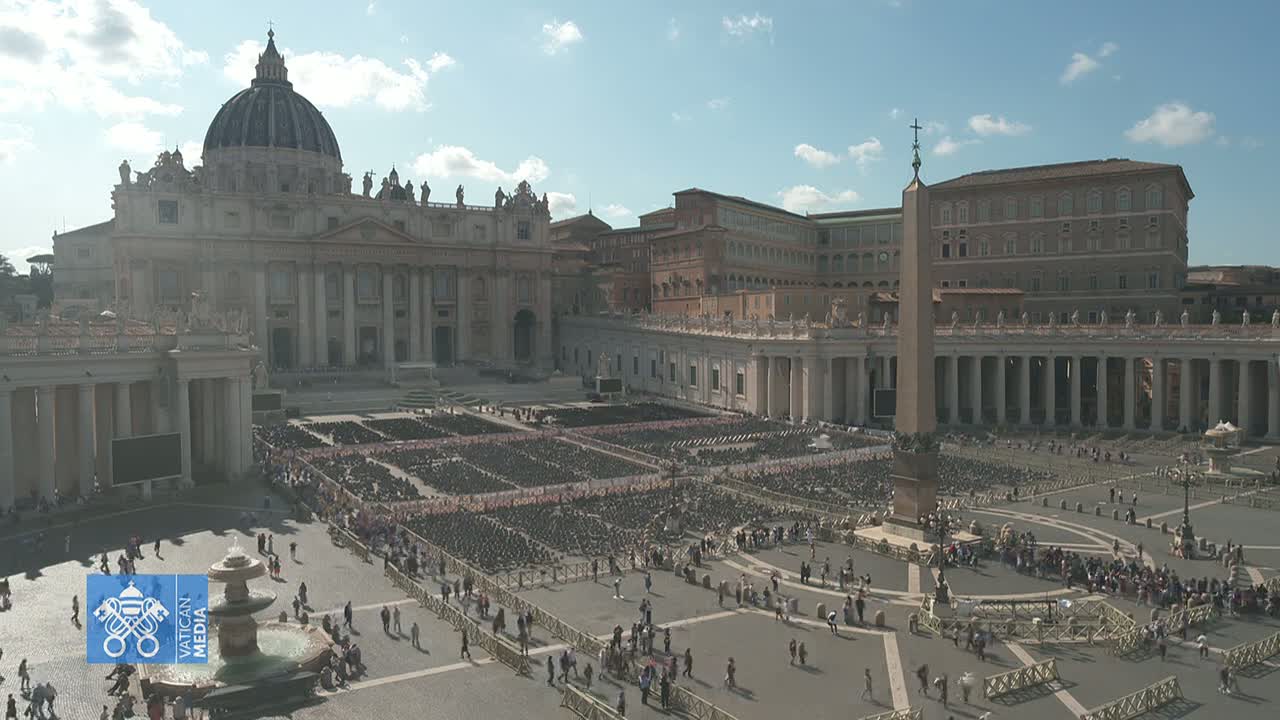 St. Peter's Square in Vatican City, filled with many people and rows of chairs under a mostly sunny sky.