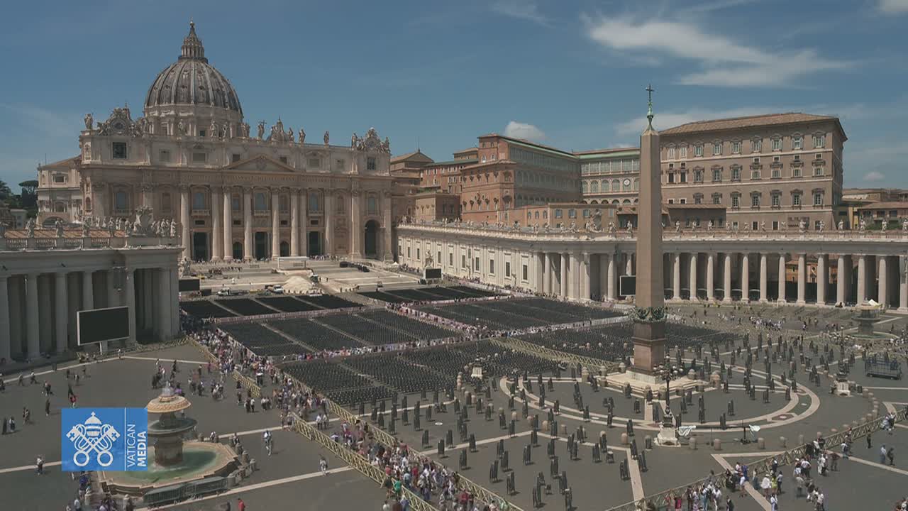 St. Peter's Basilica and St. Peter's Square in Vatican City are shown on a sunny day, with many people gathered in the square and rows of chairs set up.