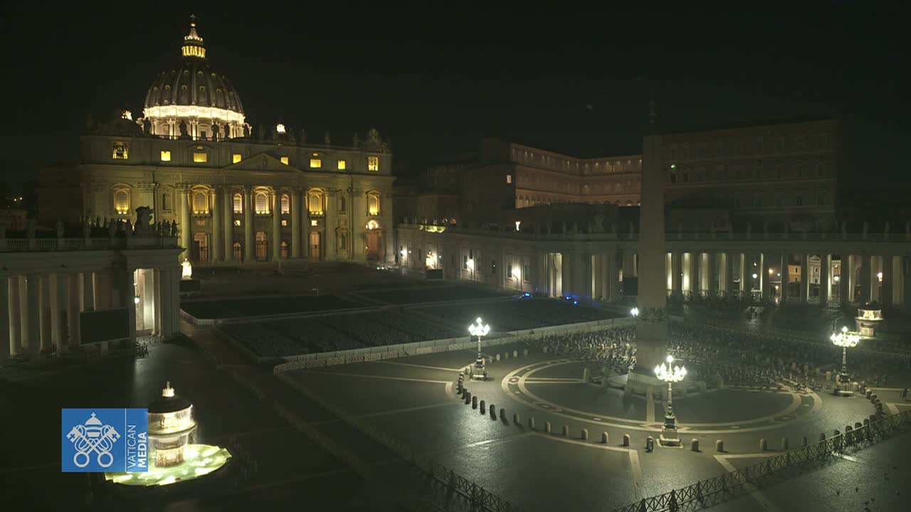 St. Peter's Basilica and St. Peter's Square are illuminated at night, with a crowd of people gathered in the square.
