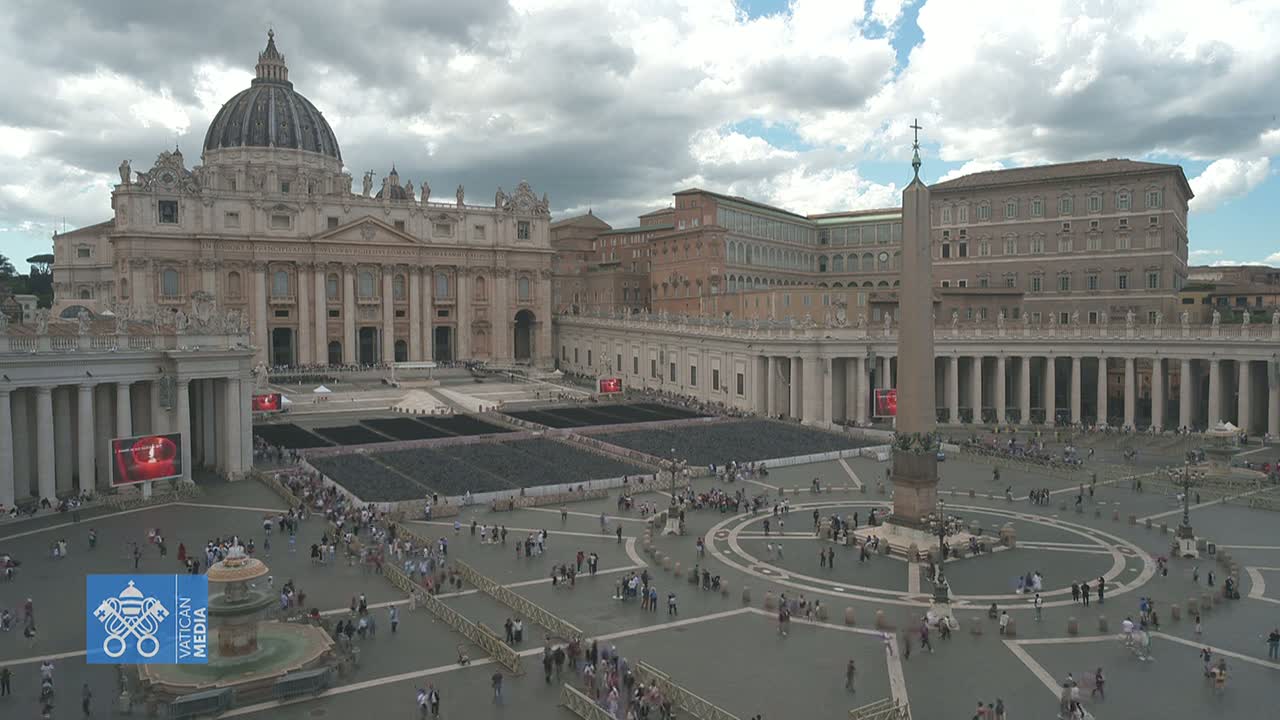St. Peter's Basilica and St. Peter's Square in Vatican City are shown on an overcast day, with many people gathered in the square.