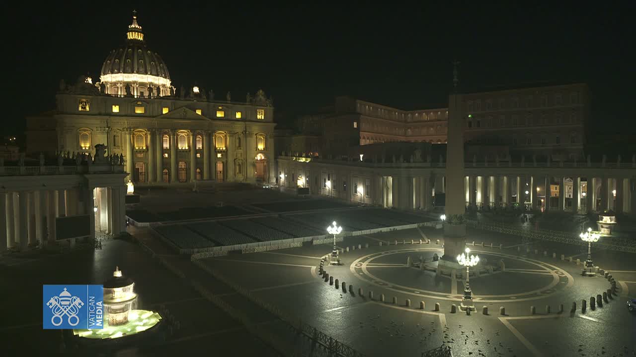 St. Peter's Basilica and St. Peter's Square are illuminated at night, with a mostly empty square and a few people visible in the distance.