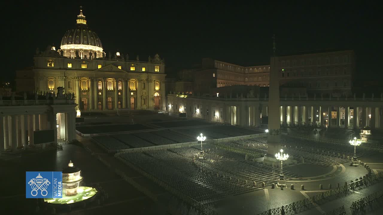 A nighttime view of St. Peter's Basilica and Square in Vatican City, showing rows of empty chairs in the square under dim lighting.