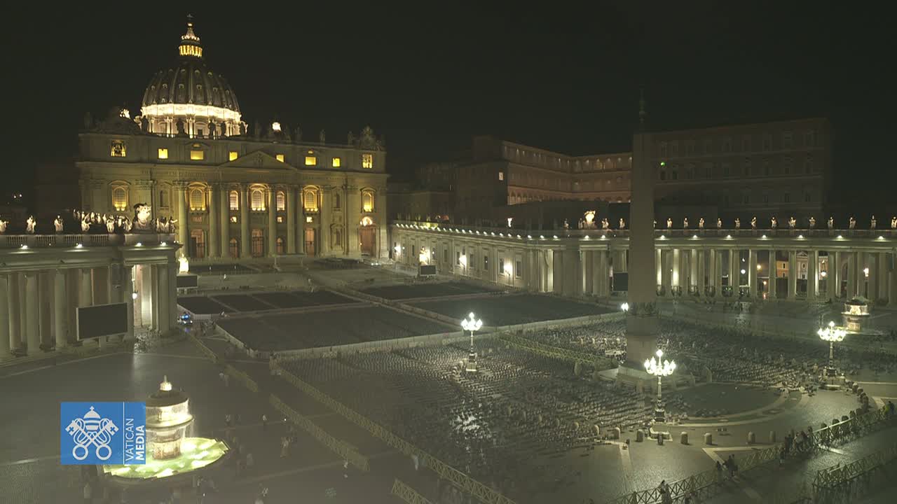 St. Peter's Basilica and square are illuminated at night, with many chairs set up in the plaza.