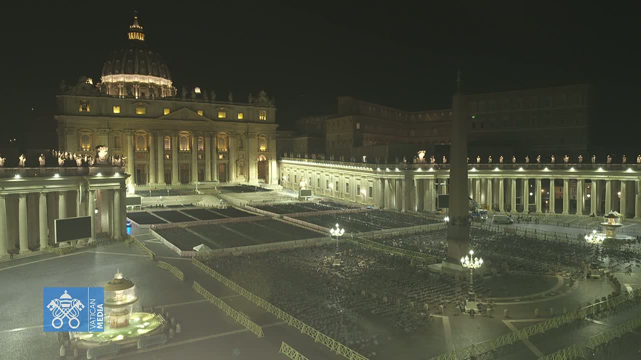 St. Peter's Basilica and Square at night, illuminated, with a large gathering of people seated in the square.