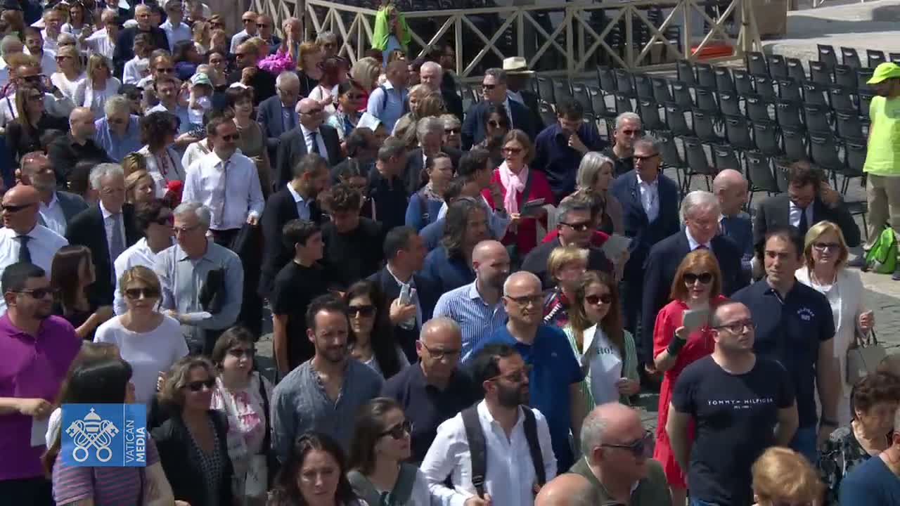A large crowd of people, mostly adults, are walking outdoors on a sunny day.