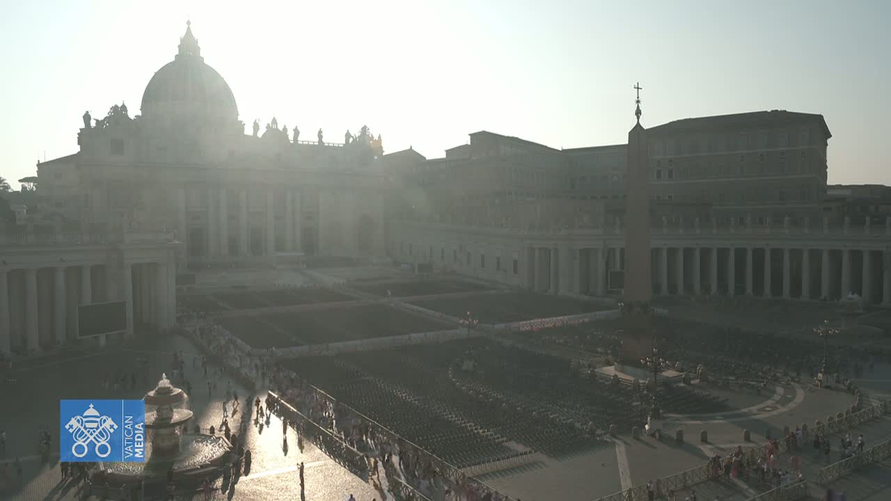 A hazy sun shines on St. Peter's Square in Vatican City, which is filled with many people and empty chairs.