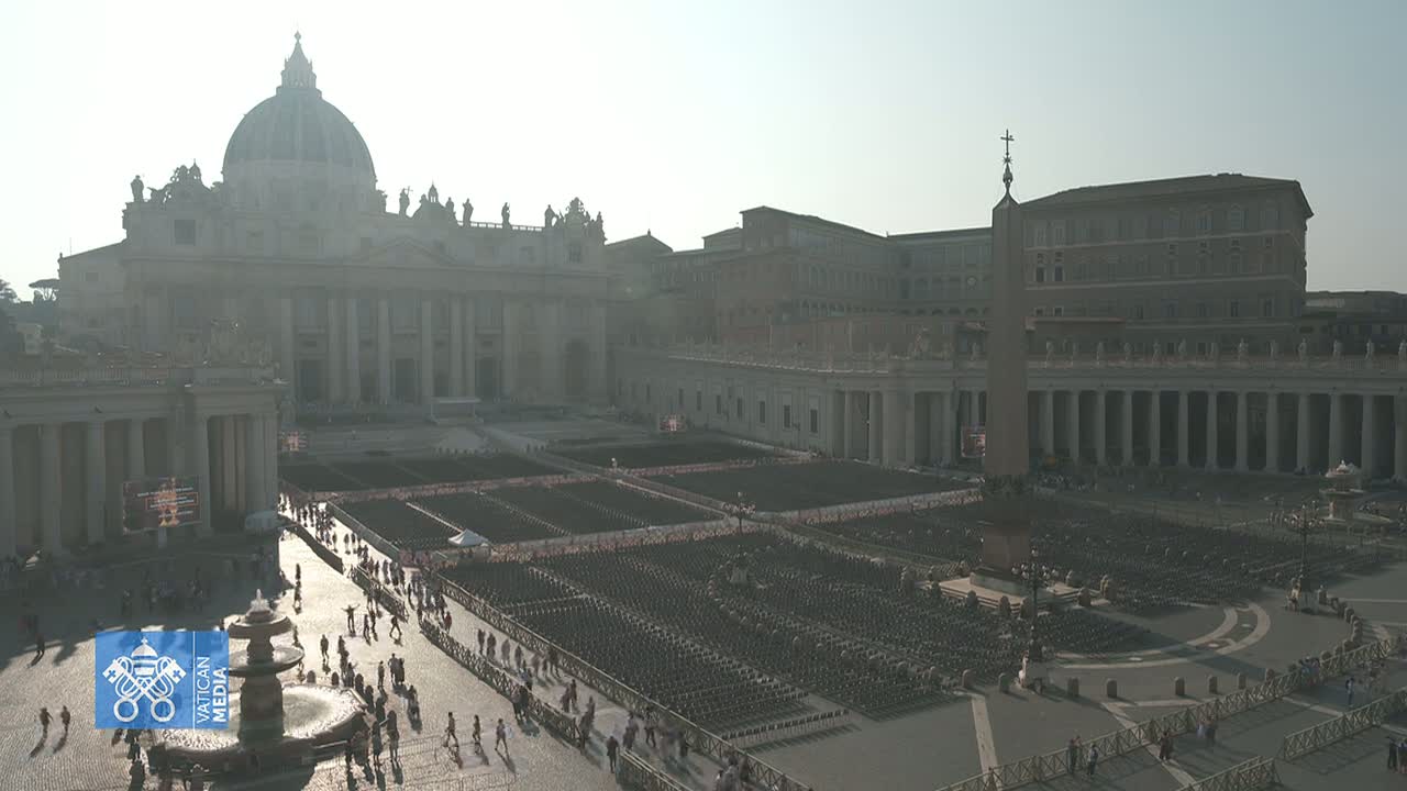 St. Peter's Basilica and St. Peter's Square in Vatican City are shown on a hazy, sunny day, with many empty chairs set up in the square and a few people walking around.