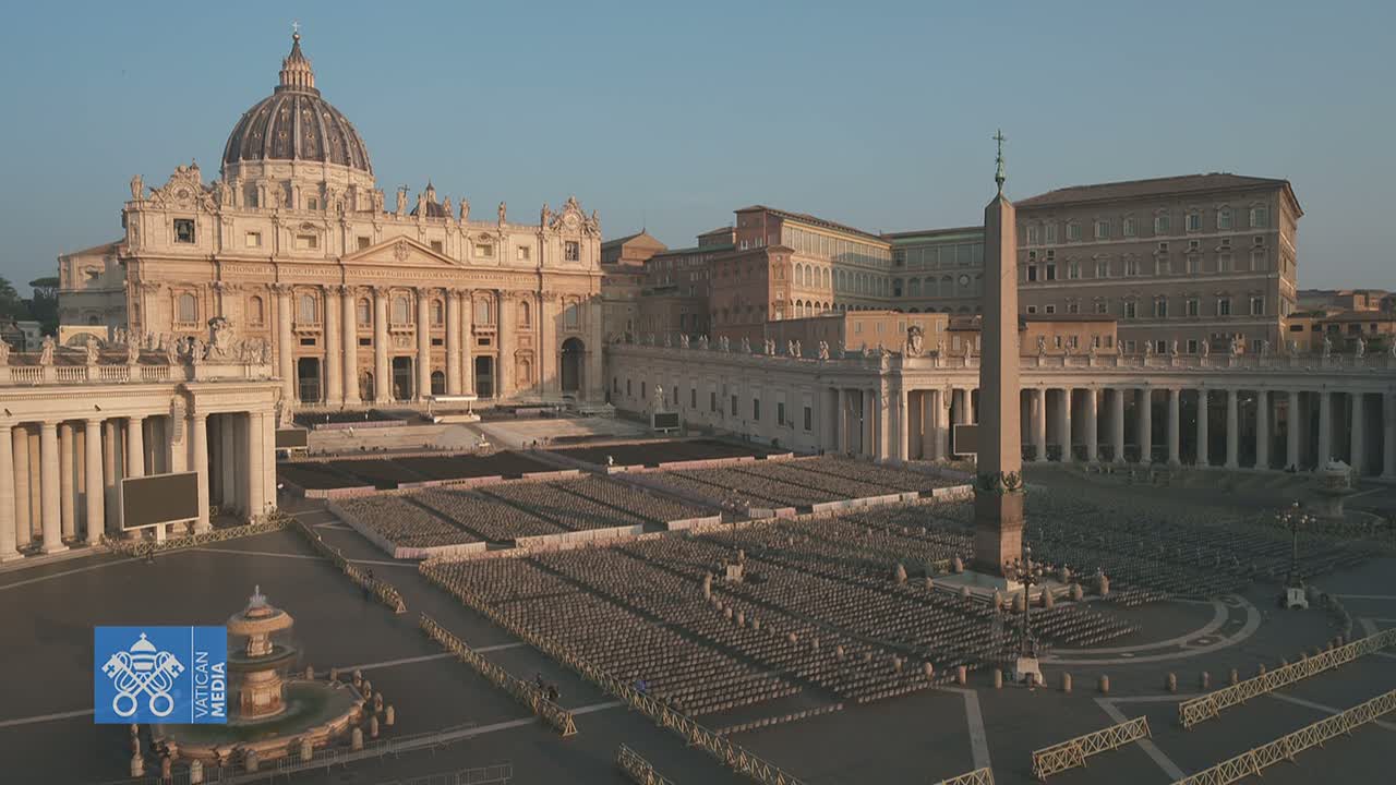 St. Peter's Basilica and St. Peter's Square in Vatican City are shown on a hazy, sunny day, with many empty chairs set up in the square and a few people walking around.