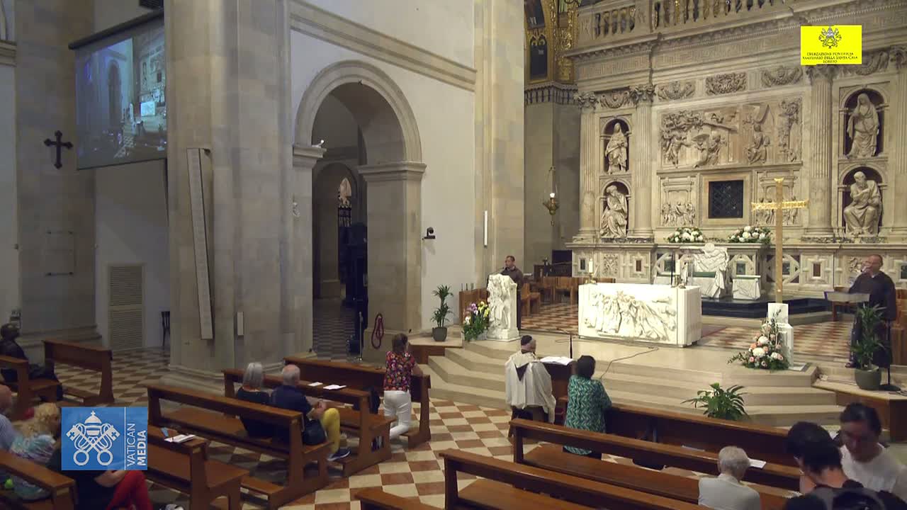A large, ornate church interior with wooden pews filled with people, a marble altar, and a projection screen showing a video.