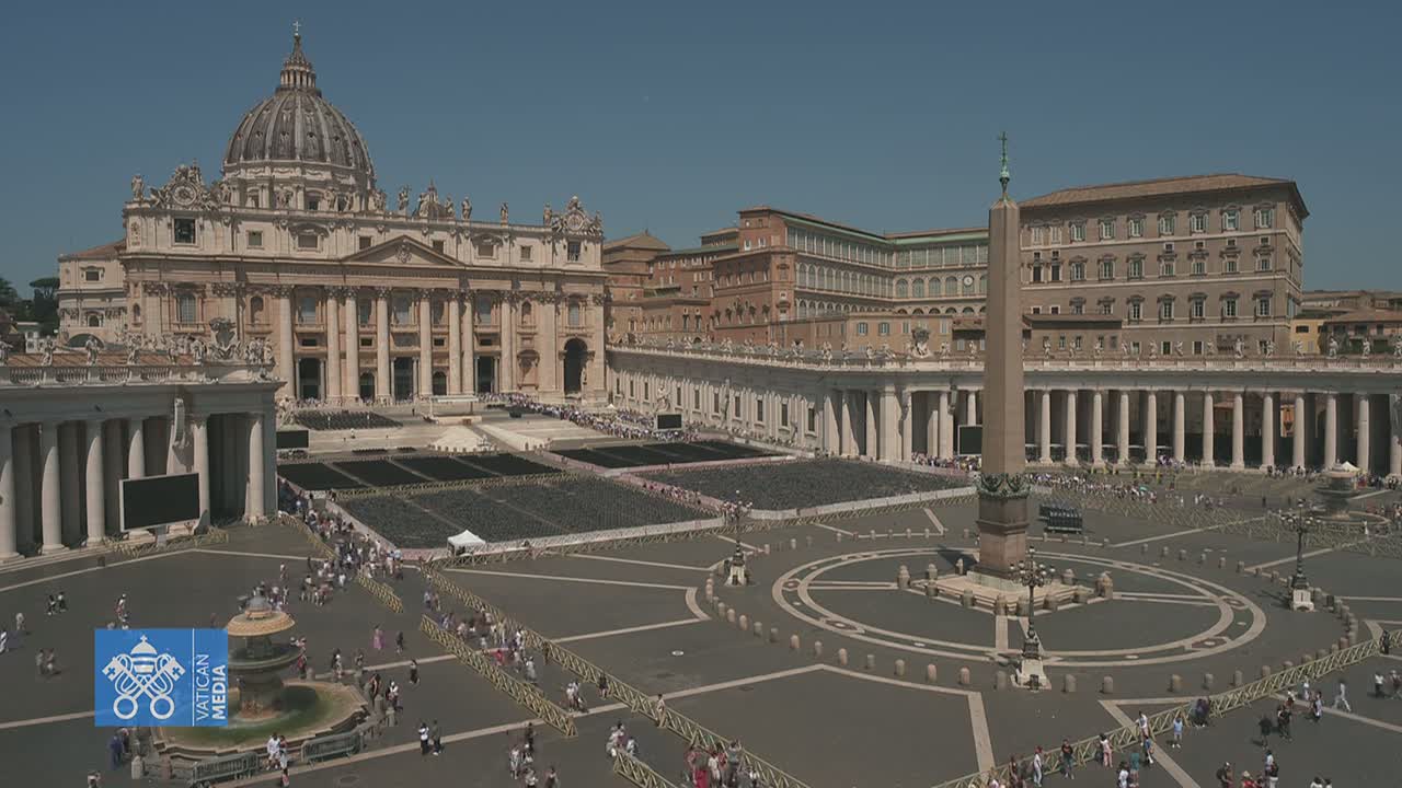 A large, sunny plaza with a basilica, obelisk, and many people stands before numerous columns and buildings.