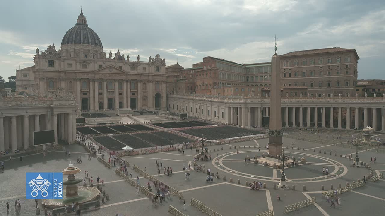 St. Peter's Basilica and St. Peter's Square in Vatican City are shown on an overcast day, with many people gathered in the square.
