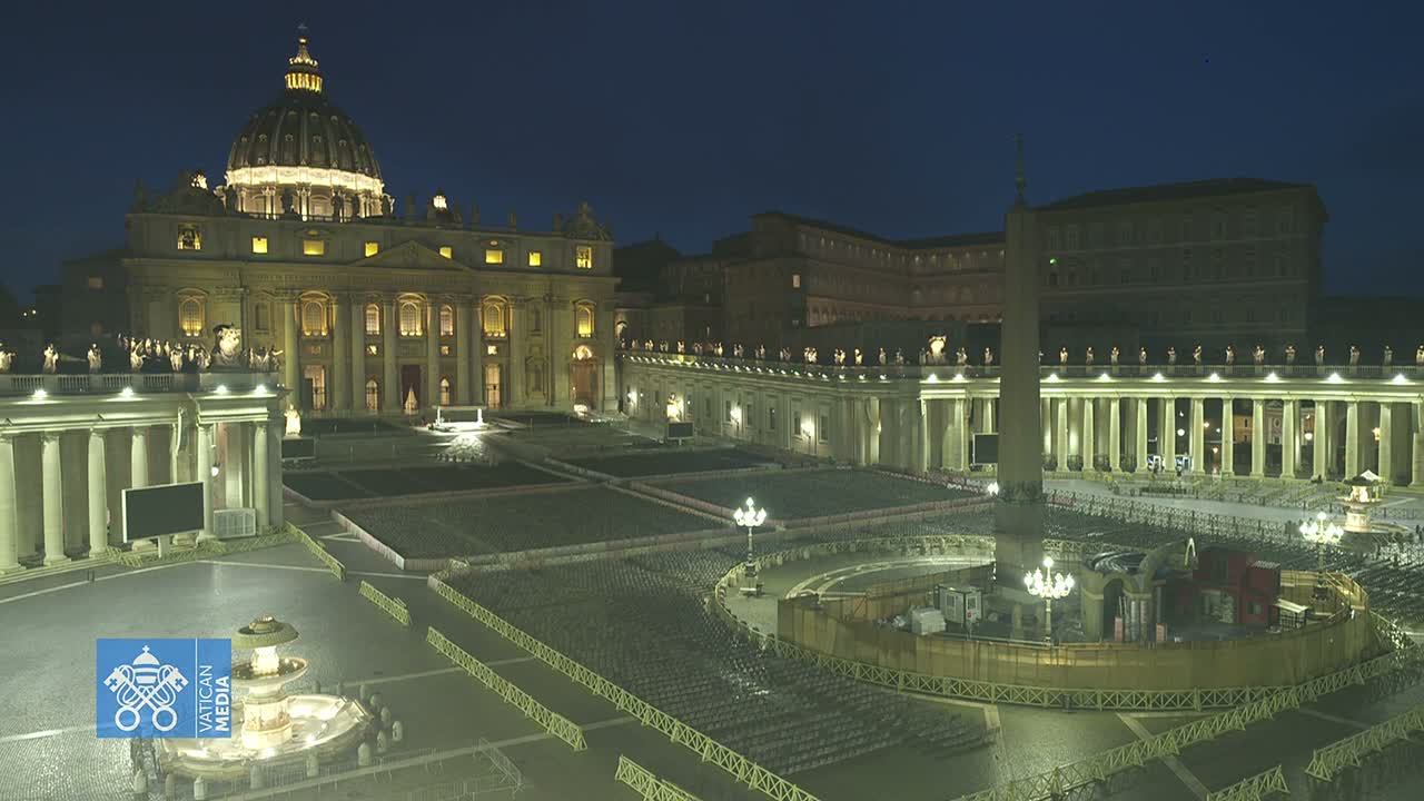 St. Peter's Basilica and Square are brightly illuminated at night under a clear, dark sky, with countless empty chairs meticulously arranged in rows across the vast paved area, centered around an obelisk and surrounded by temporary structures.