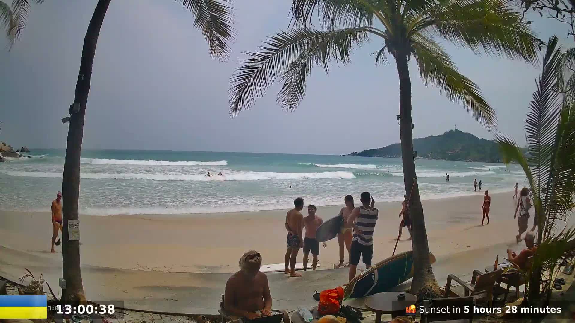 A sandy beach with gentle waves, palm trees, and several people enjoying the overcast day.