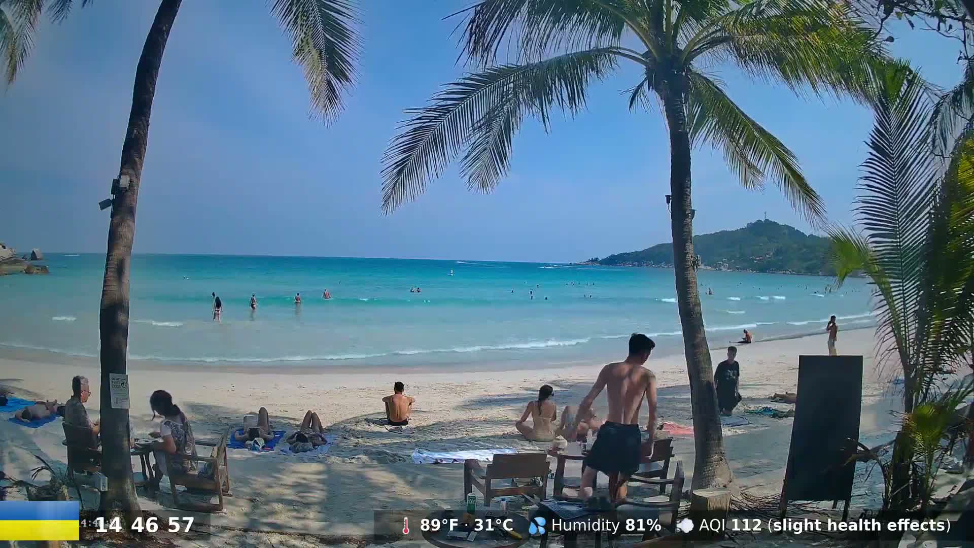 A sunny beach scene with turquoise water, palm trees, and people relaxing on the sand and in the ocean.