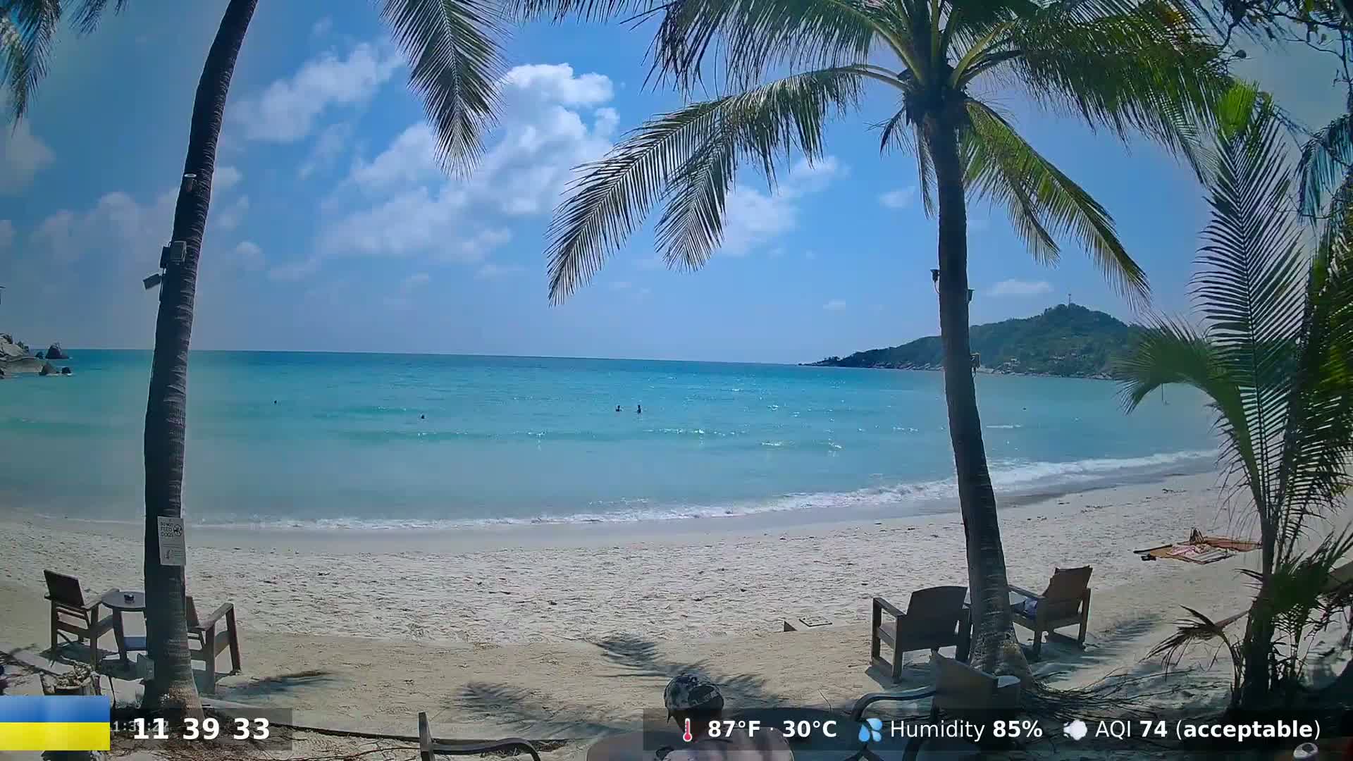A partly cloudy, sunny day at a tropical beach with calm turquoise water, palm trees, and beach chairs.