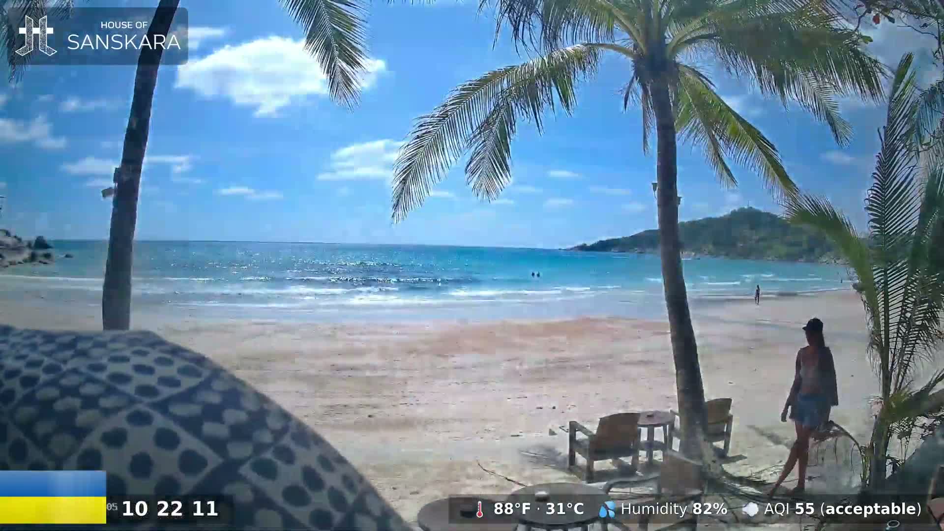 A sandy beach with palm trees, clear turquoise water, and a partly sunny sky.