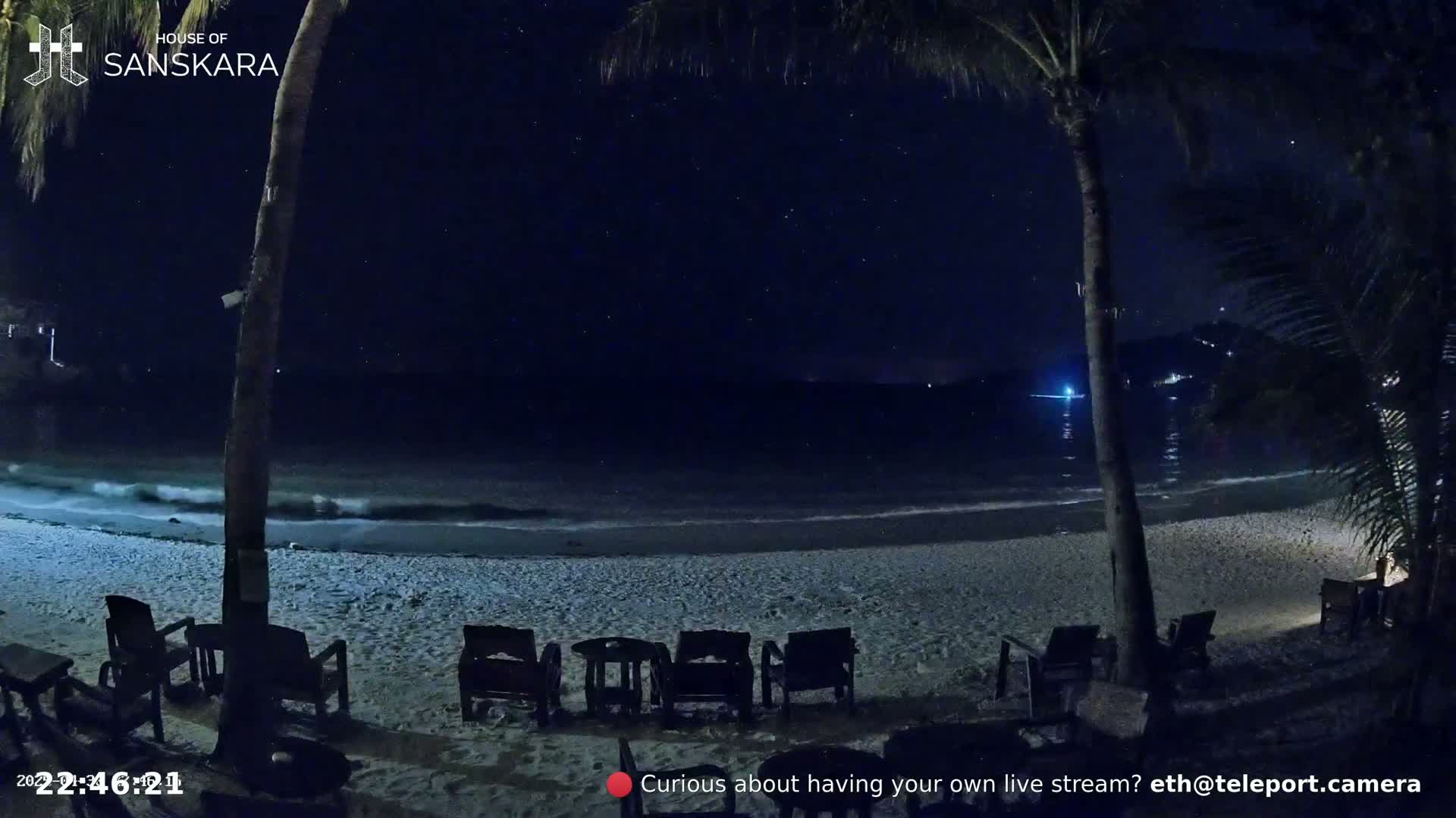 Under a starry night sky, gently lapping waves reach a sandy beach where several empty chairs sit before a calm ocean.