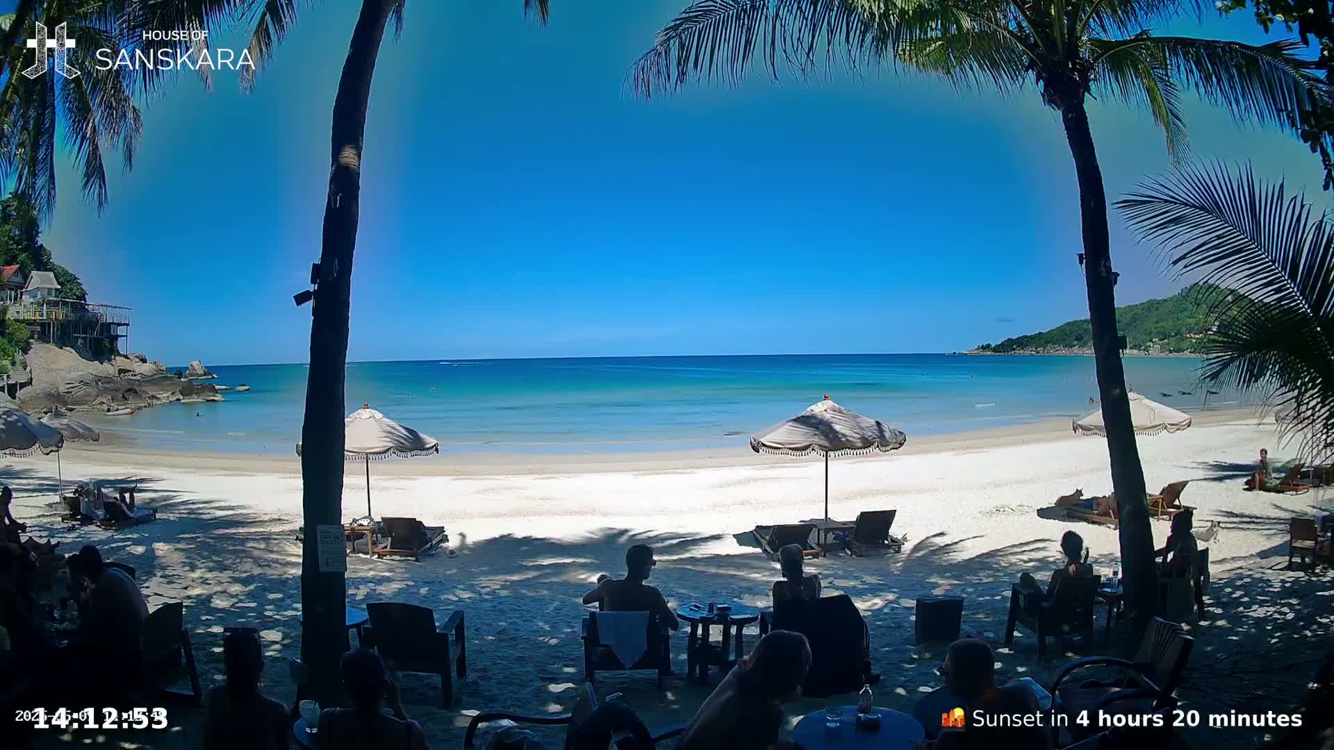 A beach with white sand, turquoise water, palm trees, and beach umbrellas under a clear blue sky.