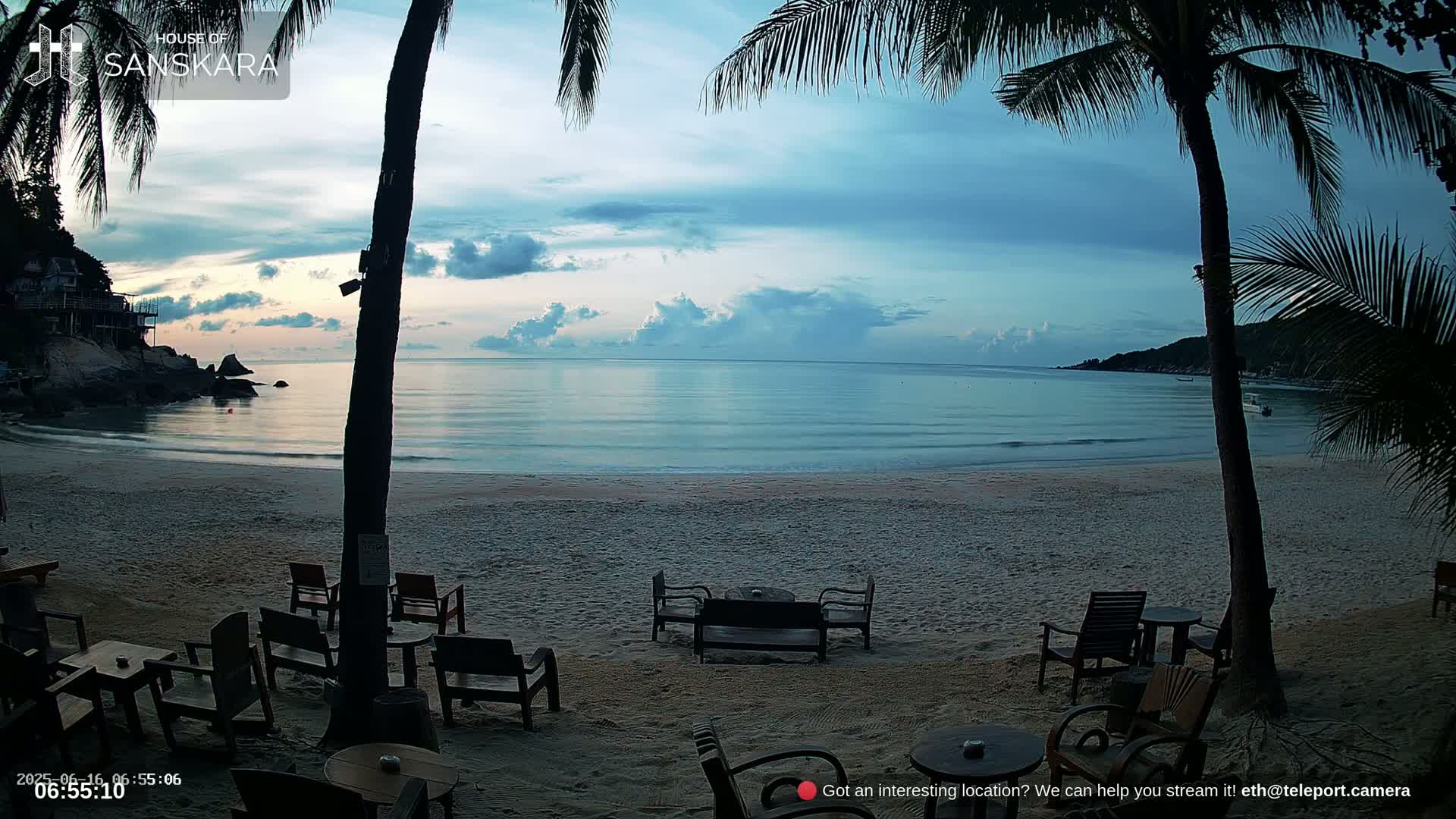A nighttime beach scene with palm trees, outdoor seating, and a calm ocean under a starry sky.